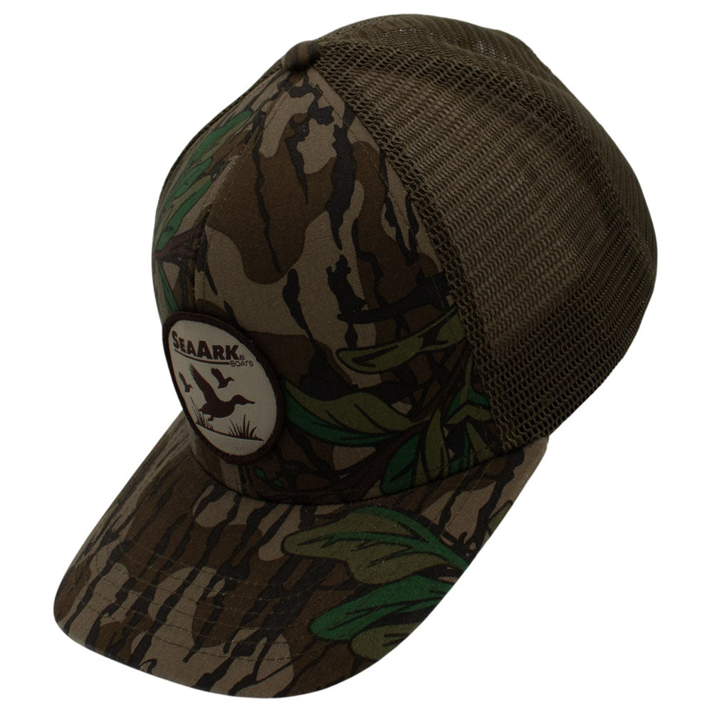 Side of a camouflage trucker hat with a brown mesh back and a circular patch on the front, shown on a plain white background.