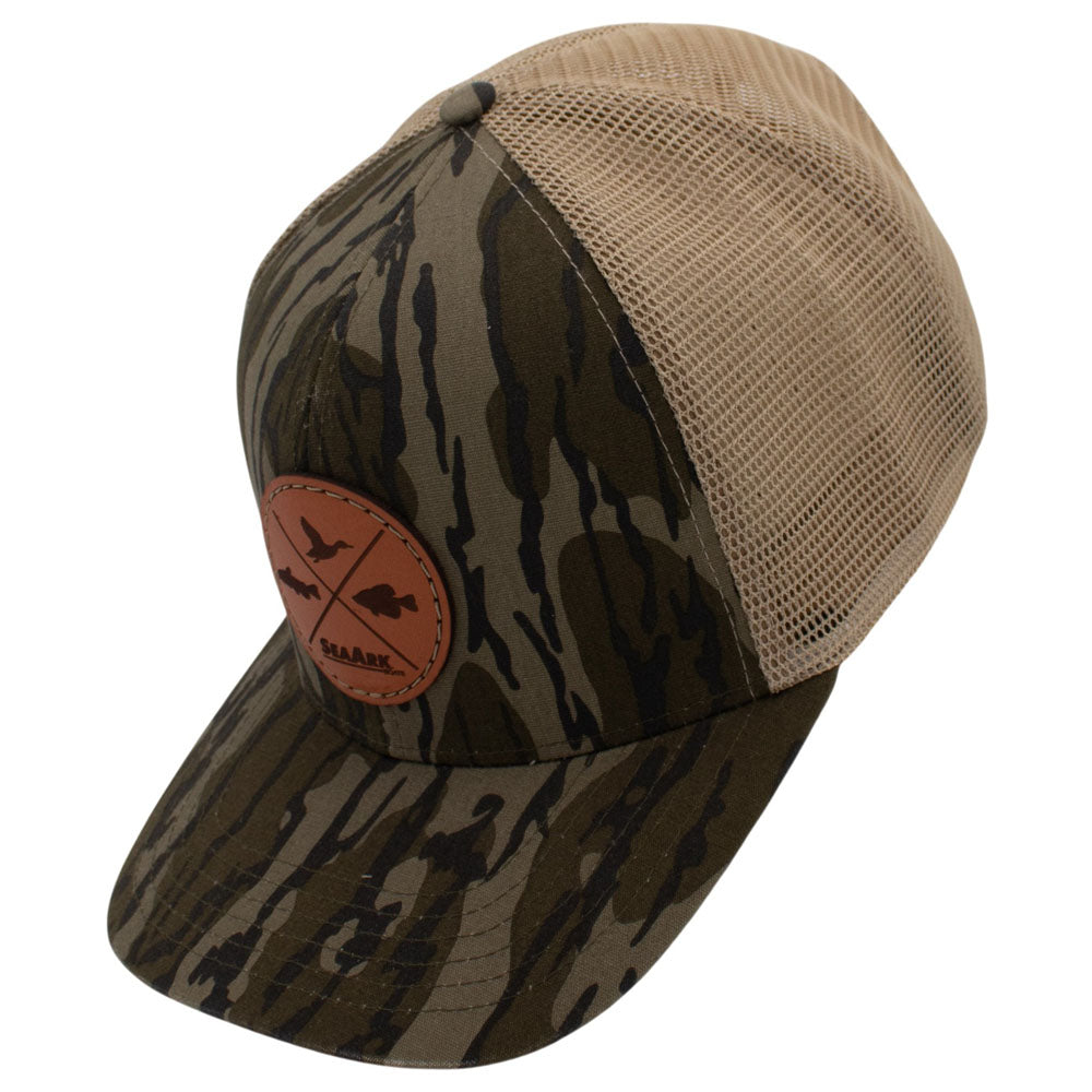 Side of a camouflage trucker hat with a tan mesh back and a brown circular patch on the front.